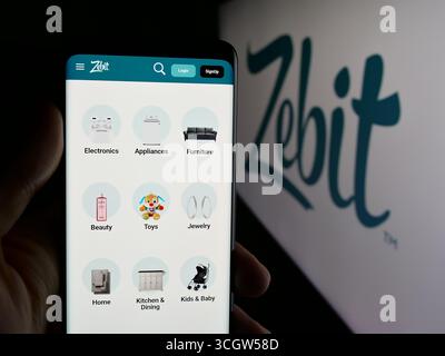 Dans cette illustration photo, une personne tient un téléphone portable avec la page Web de la société américaine de commerce électronique Zebit sur l'écran devant le logo. Banque D'Images