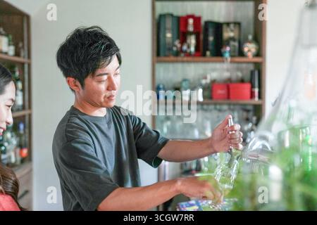 Un homme verse une boisson dans un verre. Une femme se tient derrière lui. La scène se déroule dans un bar Banque D'Images