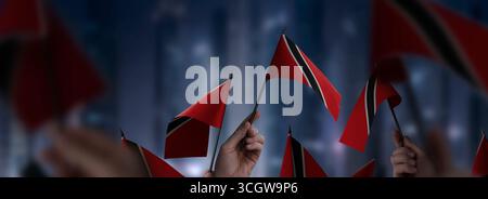 Drapeaux de Trinité-et-Tobago dans leurs mains sur un fond urbain flou Banque D'Images