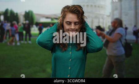 Femme exprimant la frustration devant la tour penchée de pise parmi les touristes dans un cadre urbain dynamique, capturant un mélange d'émotion et de t emblématique Banque D'Images