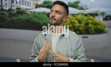 Jeune homme hispanique compte avec les doigts sur la rue de la ville entourée de paysages urbains avec des fleurs vibrantes, véhiculant la réflexion et la concentration dedans Banque D'Images