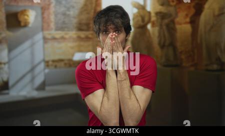 Homme en t-shirt rouge place les deux mains sur la poitrine et incline la tête tout en se tenant debout dans le bâtiment du musée ; sincérité. Banque D'Images