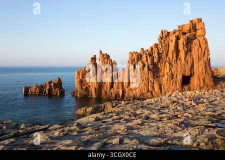 Arbatax, Tortolì, Ogliastra, Sardaigne, Italie. Falaises de porphyre rouge surplombant le rivage rocheux de la Baia delle Rocce Rosse, coucher de soleil. Banque D'Images