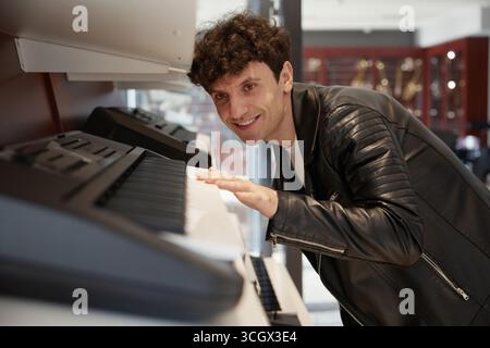 Un musicien talentueux souriant joyeusement tout en jouant d'un clavier électronique à l'intérieur d'un magasin moderne Banque D'Images