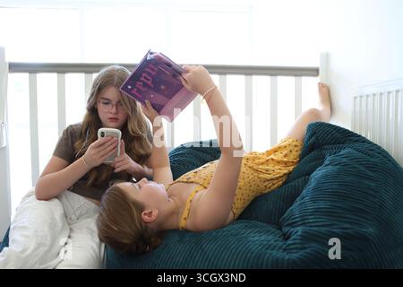 Deux filles on lit le livre autres regards sur le concept de téléphone intelligent lecture de livres d'alphabétisation screentime écran temps adolescent adolescents se détendre Banque D'Images