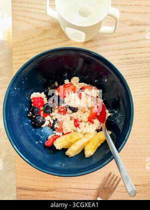 Un bol de petit-déjeuner vibrant composé de granola, de baies mélangées et de bananes, servi dans un bol bleu sur une table en bois. Bien commencer la journée Banque D'Images