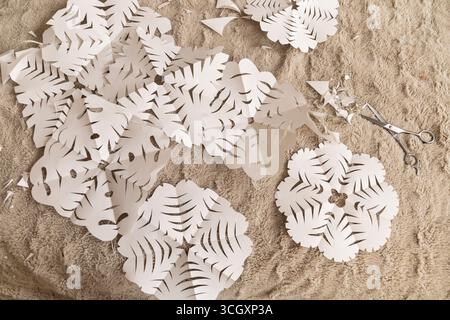 Un espace de travail confortable présente une gamme de découpes en papier blanc avec des motifs de feuilles complexes. Les ciseaux reposent à proximité, faisant allusion à un projet créatif dans Banque D'Images