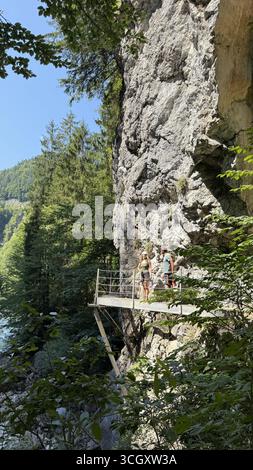 Deux randonneurs se tiennent sur une passerelle panoramique le long d'une falaise, entourée d'une forêt luxuriante. Ils ont l'air détendu et engagé, en prenant dans le naturel à couper le souffle Banque D'Images