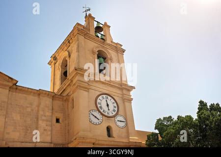 Clocher d'une église catholique avec trois cadrans d'horloge conçus différemment montrant des heures différentes dans un ciel dégagé. Banque D'Images