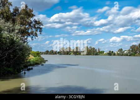 Longue exposition capture les eaux sereines de Guadalquivir, reflétant le ciel et créant une atmosphère tranquille à Coria del Río. Banque D'Images