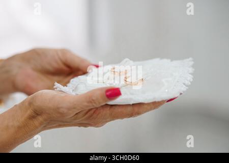 Gros plan des mains d'une femme mûre tenant doucement un oreiller d'anneau de dentelle blanche avec deux bandes de mariage dorées, symbolisant l'amour, l'engagement et marit Banque D'Images