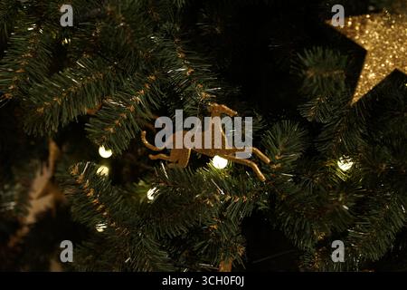 Un ornement de cheval en or orne un sapin de Noël, entouré d'accents rouge foncé et noir, évoquant le luxe et l'atmosphère festive Banque D'Images