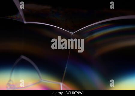 Plan macro d'un bord de bulle de savon avec couleurs arc-en-ciel irisées et mouvement liquide sur fond noir Banque D'Images