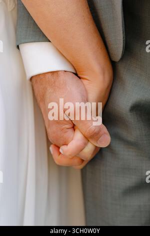 L'image intime en gros plan capture un couple tenant la main serrée pendant leur cérémonie de mariage. Le marié porte un costume, et la mariée est dans un blanc Banque D'Images