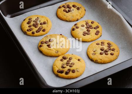Biscuits aux pépites de chocolat fraîchement cuits sur une plaque de cuisson avec du papier sulfurisé Banque D'Images