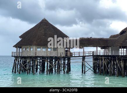 Une pittoresque jetée en bois et un restaurant aux toits de chaume s'étendent sur les eaux turquoises de l'océan Indien, vues d'un sable blanc immaculé Banque D'Images