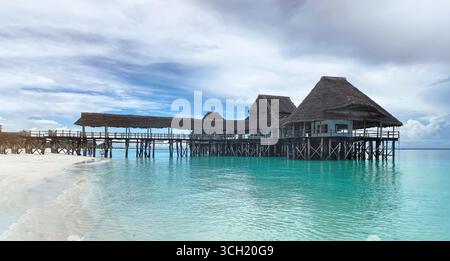 Une pittoresque jetée en bois et un restaurant aux toits de chaume s'étendent sur les eaux turquoises de l'océan Indien, vues d'un sable blanc immaculé Banque D'Images