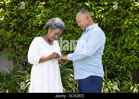 Couple senior échangeant des anneaux dans le jardin, partageant un moment joyeux ensemble Banque D'Images