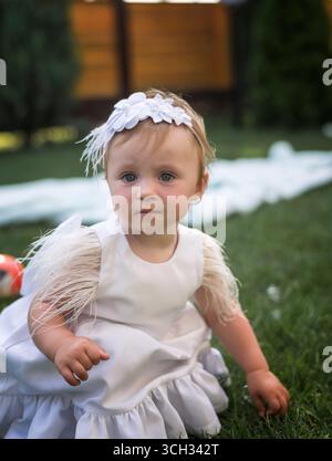 Portrait de petite fille mignonne, adorable, blonde avec les yeux bleus, portant une robe blanche avec coiffe blanche Banque D'Images