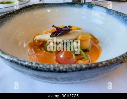 Un plat soigneusement plaqué sur une assiette blanche, servi sur une table avec des draps blancs dans un restaurant gastronomique. Le menu propose des plats raffinés avec des couleurs vives Banque D'Images
