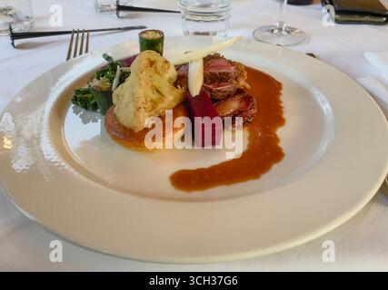 Un plat soigneusement plaqué sur une assiette blanche, servi sur une table avec des draps blancs dans un restaurant gastronomique. Le menu propose des plats raffinés avec des couleurs vives Banque D'Images