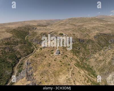 Vue aérienne d'une église en pierre perchée précairement sur une colline au milieu d'un paysage d'herbes dorées et de terrain accidenté, église de Vahramashen, province d'Aragatsotn, Arménie. Banque D'Images