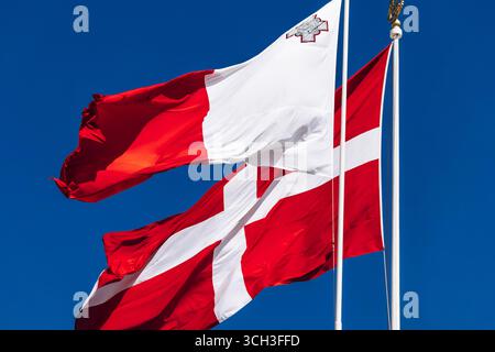 Le drapeau national de Malte et le drapeau de l'ordre souverain militaire de Malte agitant sur des mâts de drapeau contre un ciel bleu clair. Banque D'Images