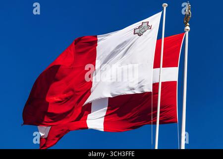 Le drapeau national de Malte et le drapeau de l'ordre souverain militaire de Malte agitant sur des mâts de drapeau contre un ciel bleu clair. Banque D'Images