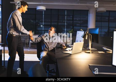 Célébrant le succès d'un projet, les professionnels divers d'affaires serrant la main au bureau la nuit Banque D'Images