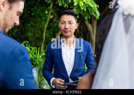 Homme asiatique en costume bleu tenant la tablette à la cérémonie de mariage en plein air Banque D'Images