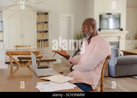 Homme senior visioconférence sur ordinateur portable à la maison, discutant des documents sur la table Banque D'Images
