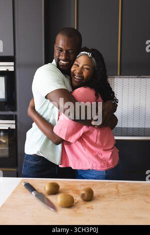 couple embrassant joyeusement dans la cuisine avec des kiwis frais sur le comptoir en bois, à la maison Banque D'Images