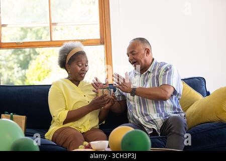 Échange de cadeaux, couple senior afro-américain partageant un moment joyeux sur le canapé Banque D'Images