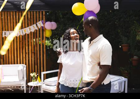 À la fête, couple heureux embrassant avec des expressions joyeuses célébrant l'anniversaire dans le jardin Banque D'Images