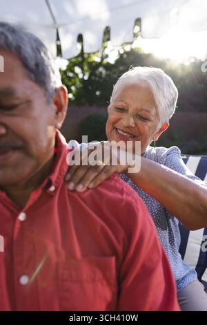 Femme senior donnant massage des épaules à l'homme dans le jardin, à la fois souriante et détendue Banque D'Images