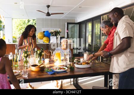 Partager le rire et la conversation, famille diversifiée ayant le repas ensemble dans le jardin autour de la table Banque D'Images