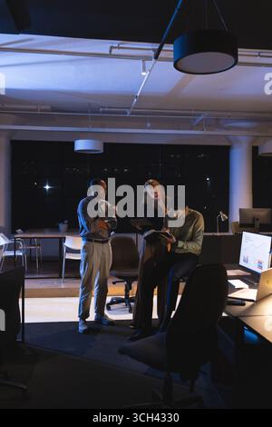 Au bureau la nuit, les professionnels des affaires examinent des documents et collaborent ensemble Banque D'Images