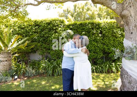 Couple senior embrassant sous l'arbre dans le jardin, profitant d'un moment paisible ensemble Banque D'Images