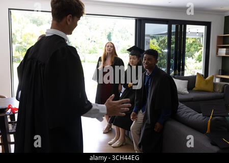Étudiants diplômés en casquettes et robes célébrant ensemble à la maison Banque D'Images