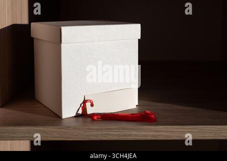 Boîte blanche et carte vierge avec pampille rouge affichée sur une étagère en bois Banque D'Images