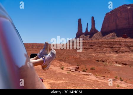 Pieds avec des baskets sur la fenêtre de la voiture avec Monument Valley en arrière-plan Banque D'Images