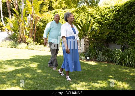 Couple senior marchant ensemble dans le jardin ensoleillé, profitant de temps de loisirs en plein air Banque D'Images