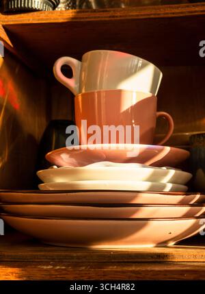 Tasses à café roses et blanches posées sur une pile de soucoupes, éclairées par la lumière chaude du soleil filtrant à travers une fenêtre, créant un atmos confortable et nostalgique Banque D'Images