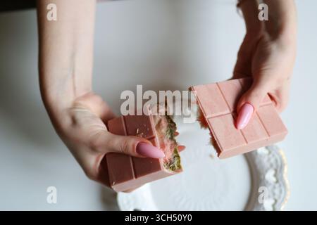 Gros plan des mains cassant la barre de chocolat rose avec matcha et garniture de crème. Banque D'Images