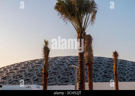 Émirats arabes Unis - Abu Dhabi - Louvre Abu Dhabi - palmiers rapprochés silhouettés contre le dôme à motifs au coucher du soleil Banque D'Images