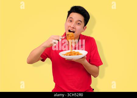 homme appréciant un repas de spaghetti avec une expression joyeuse sur fond jaune vif Banque D'Images