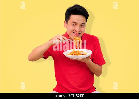 homme appréciant un repas de spaghetti avec une expression joyeuse sur fond jaune vif Banque D'Images