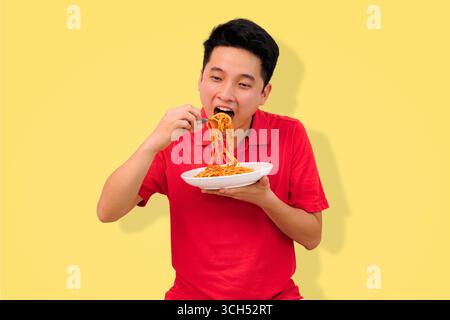 homme appréciant un repas de spaghetti avec une expression joyeuse sur fond jaune vif Banque D'Images