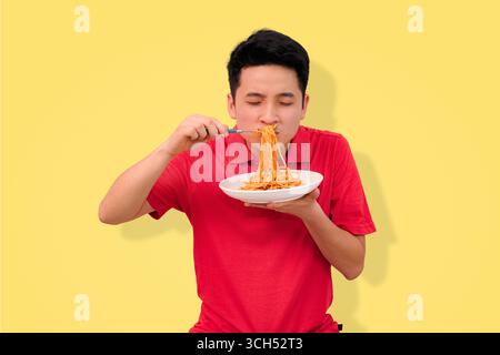 homme appréciant un repas de spaghetti avec une expression joyeuse sur fond jaune vif Banque D'Images