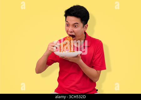 homme appréciant un repas de spaghetti avec une expression joyeuse sur fond jaune vif Banque D'Images